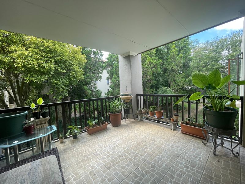 A covered balcony featuring tiled flooring and a railing, offering a pleasant outdoor space with views of surrounding greenery.