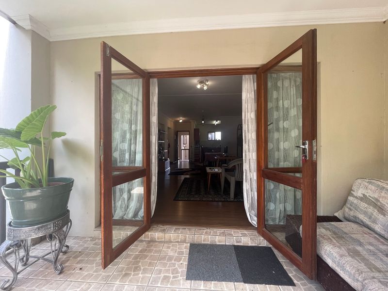 A covered patio area featuring tiled flooring and double wooden doors providing access to the interior living space.
