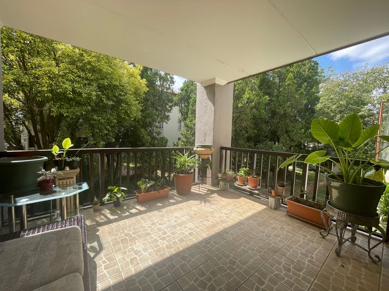 A covered balcony featuring tiled flooring and a protective railing, offering a pleasant outdoor space with views of surrounding greenery.