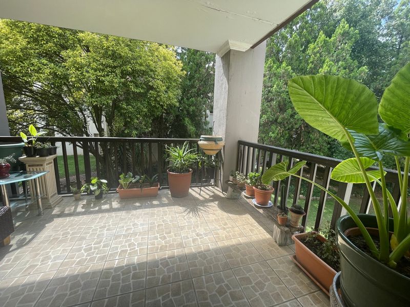 A covered balcony featuring tiled flooring and a timber balustrade, offering a pleasant outdoor space with views of the surrounding greenery.