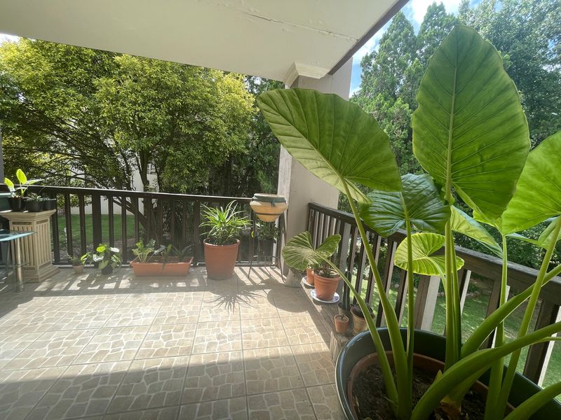 A covered balcony featuring tiled flooring and a timber balustrade, overlooking a lush garden area.
