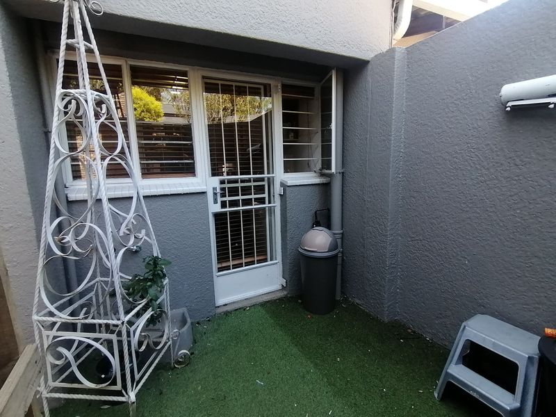 A small, private rear courtyard area featuring artificial grass, a secure entrance door with security gate, and window security bars.