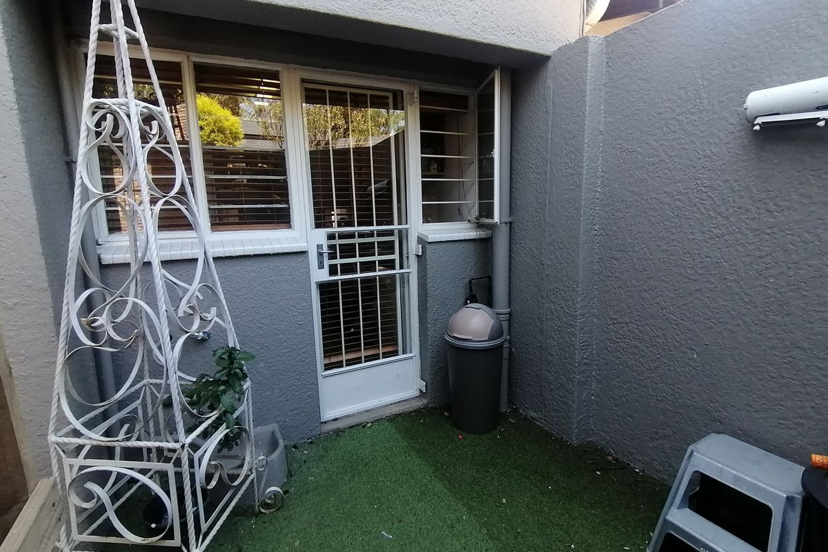 A small, private rear courtyard area featuring artificial grass, a secure entrance door with security gate, and window security bars.