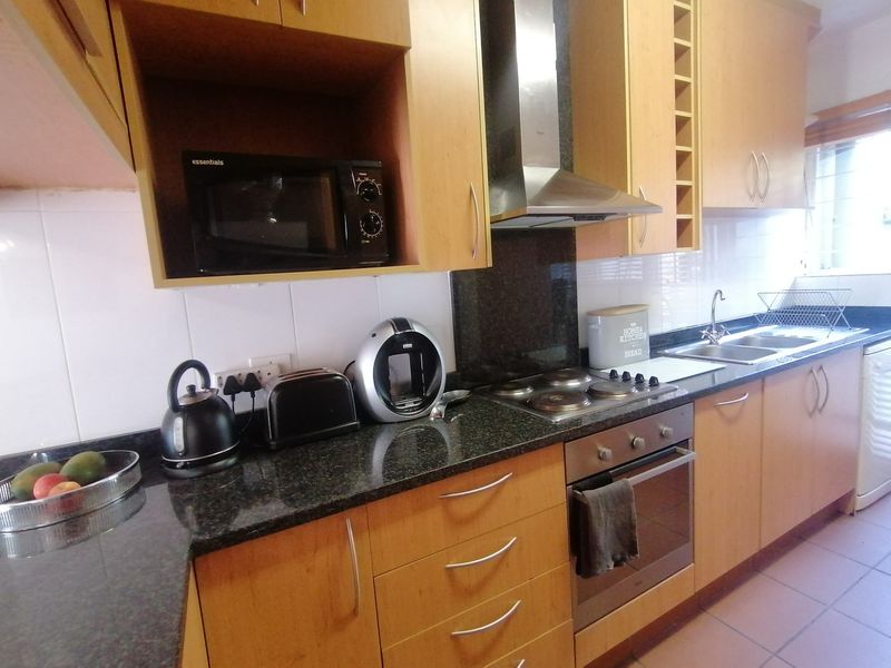 A functional kitchen featuring light wood-finish cabinetry, dark granite countertops, a built-in oven with gas hob, and a stainless steel extractor fan.