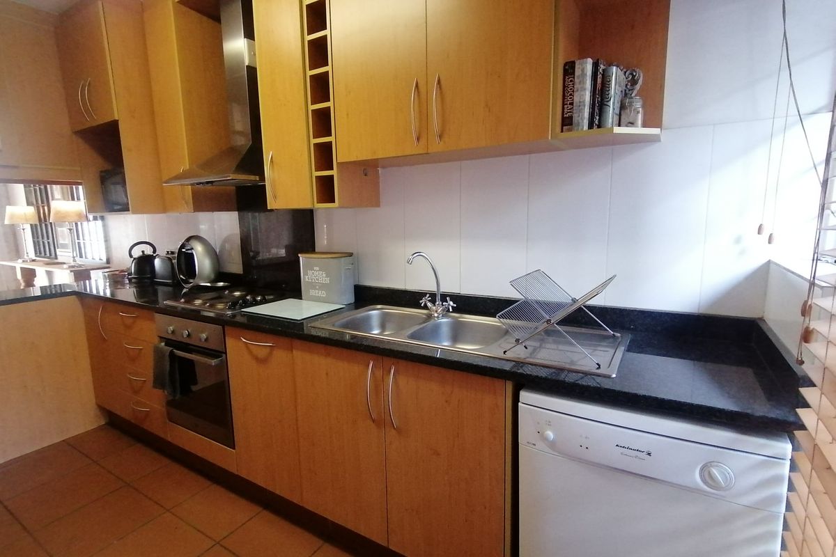 A functional kitchen featuring wooden cabinetry, granite countertops, a stainless steel double sink, and built-in cooking appliances with tiled flooring.