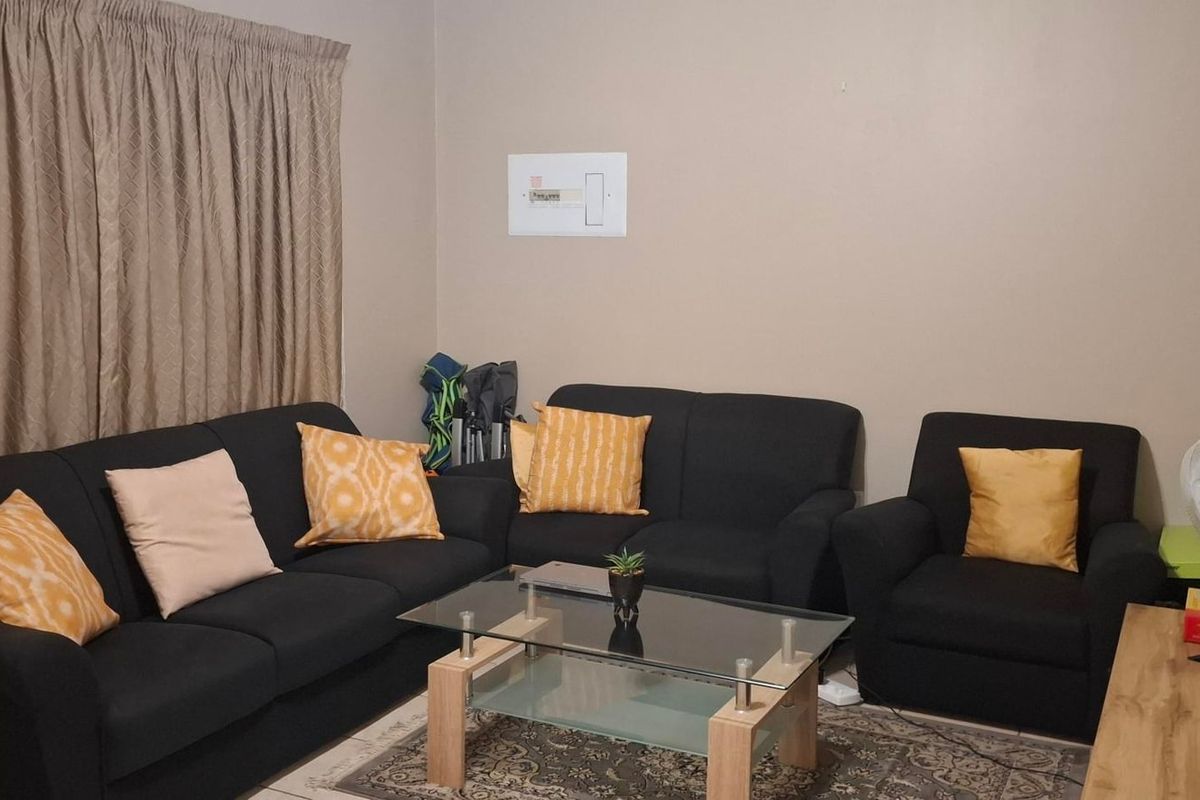 A standard living room featuring neutral wall paint, floor-length curtains, and a visible electrical distribution board.