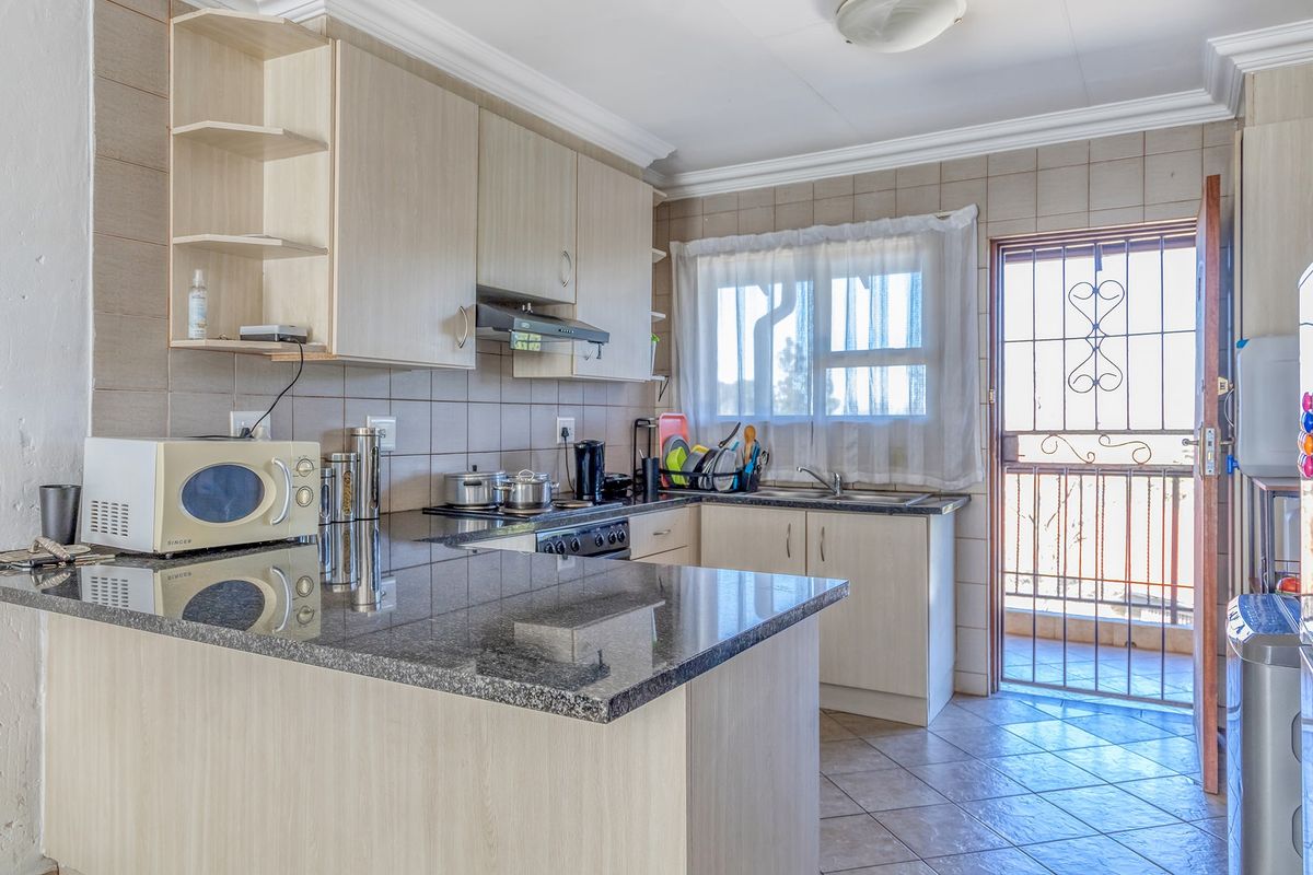 Functional kitchen featuring granite countertops, ample built-in cabinetry, tiled backsplash, and direct access to an outdoor balcony through a secure door.