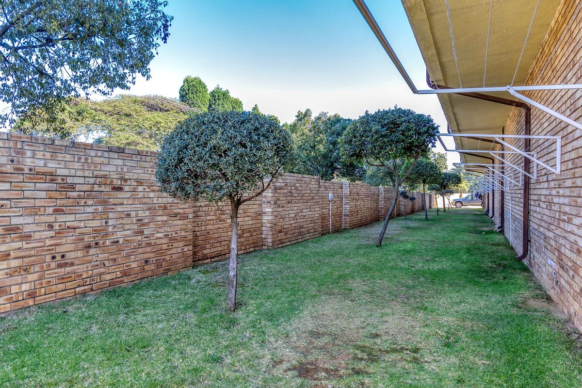 A well-maintained rear garden area featuring a long brick boundary wall, manicured trees, and a practical wall-mounted clothesline attached to the building exterior.