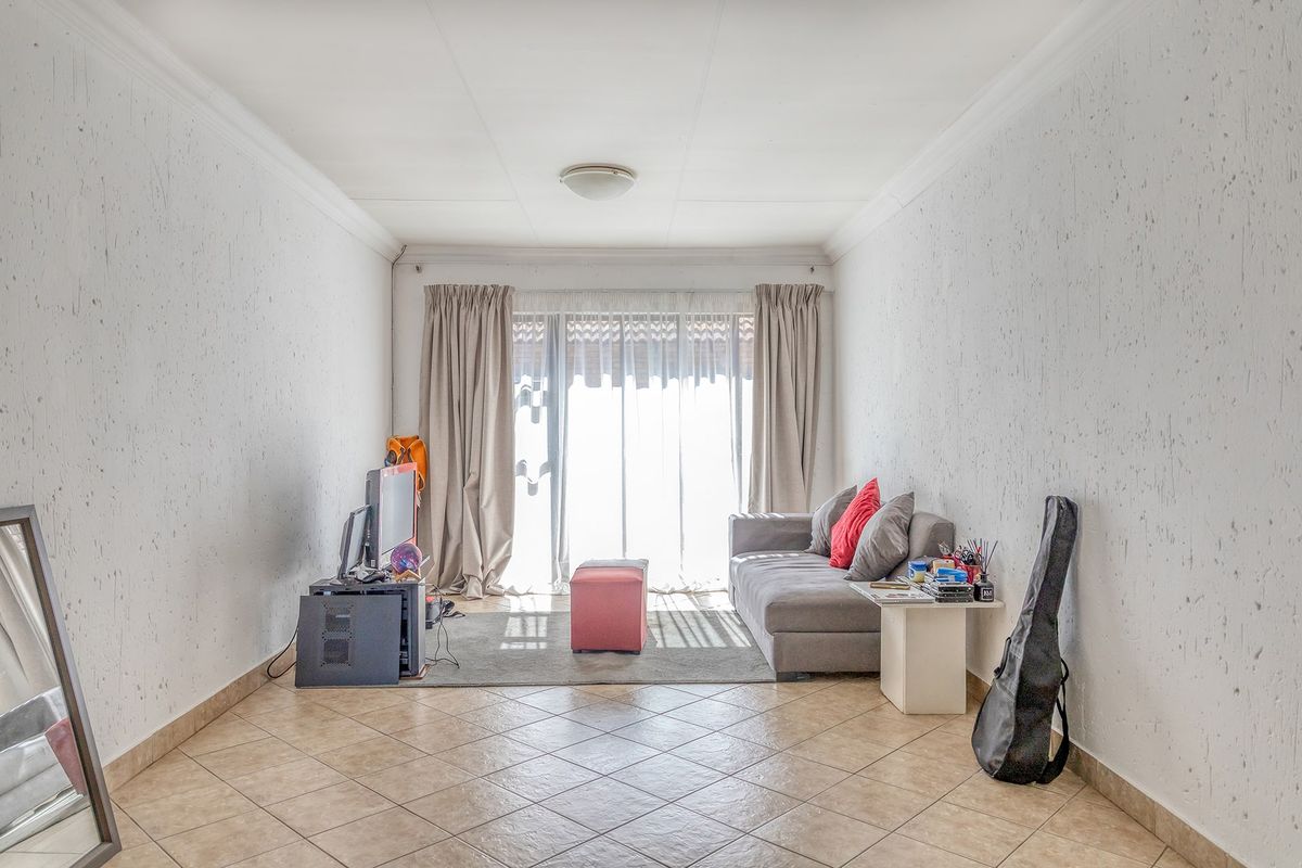 A living room featuring tiled flooring, textured walls, and a sliding glass door providing natural light and access to the exterior.