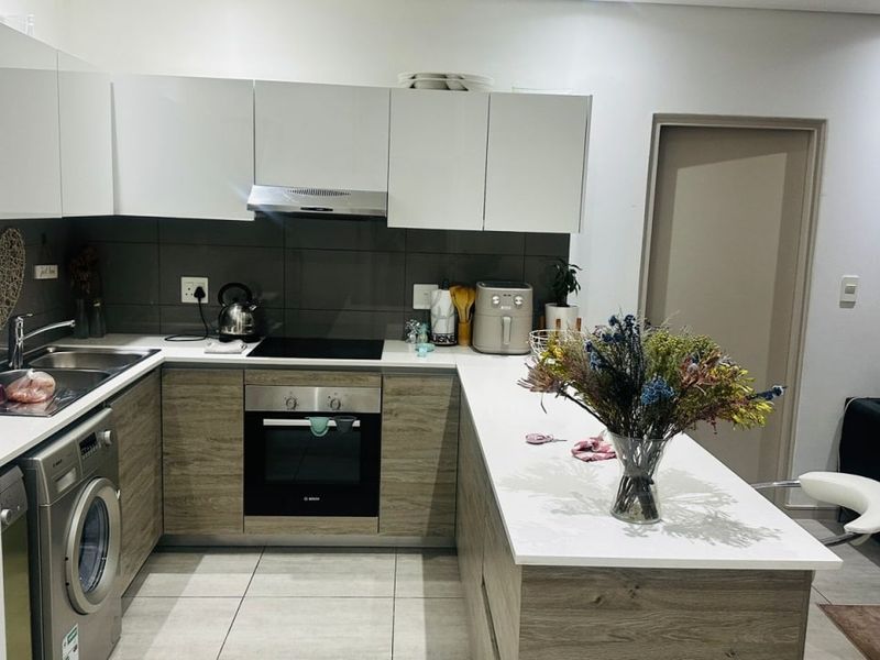 Modern kitchen featuring sleek white and wood-grain cabinetry, integrated oven, electric hob, and a functional breakfast bar with stone countertops.
