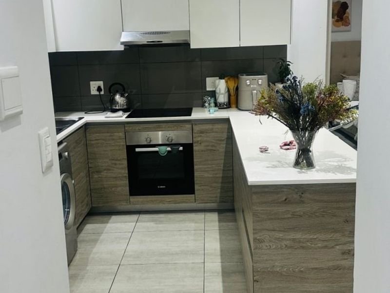 Modern kitchen featuring wood-grain and white cabinetry, stone countertops, integrated appliances, and sleek tiled flooring in an open-plan layout.