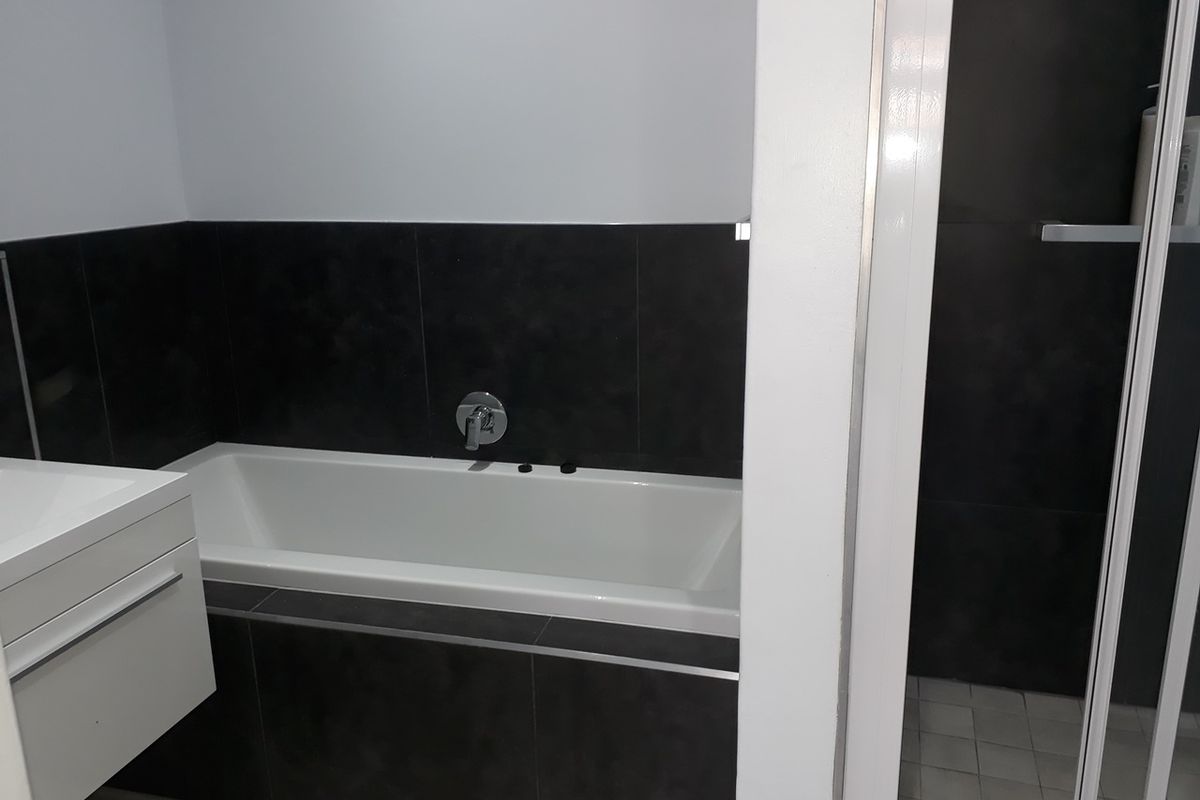 Modern bathroom featuring a built-in bathtub with dark tiled surround, wall-mounted mixer, and a separate shower enclosure with a vanity unit.