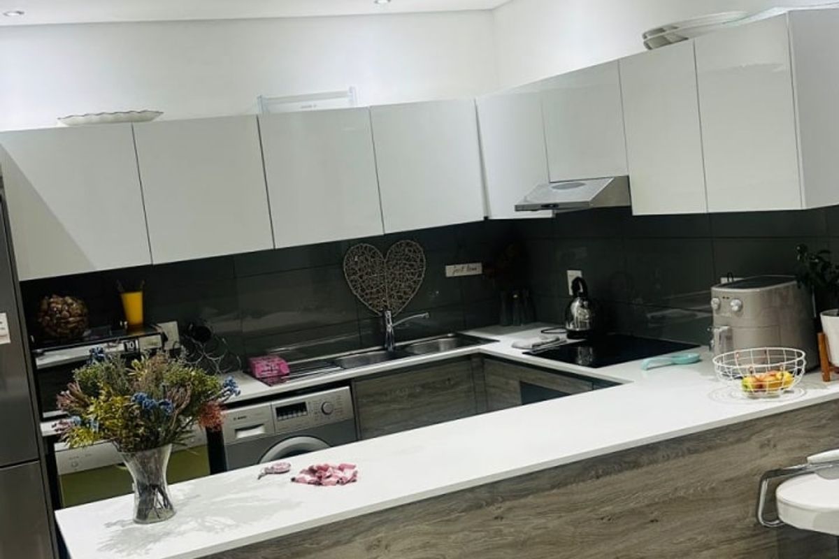 Modern kitchen featuring white gloss cabinetry, wood-look breakfast bar, stone-look countertops, dark glass splashback, and recessed downlighting.