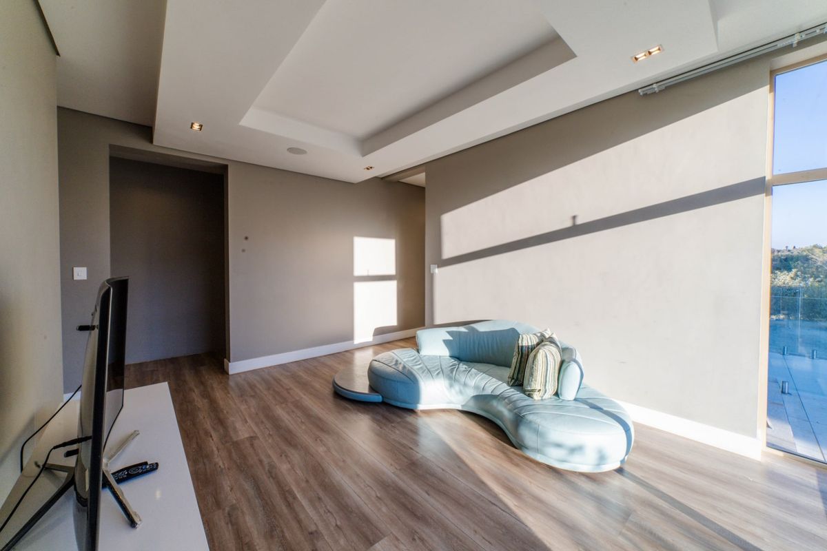 A modern living room featuring recessed ceiling details, warm laminate flooring, and a large glass door providing natural light and outdoor access.
