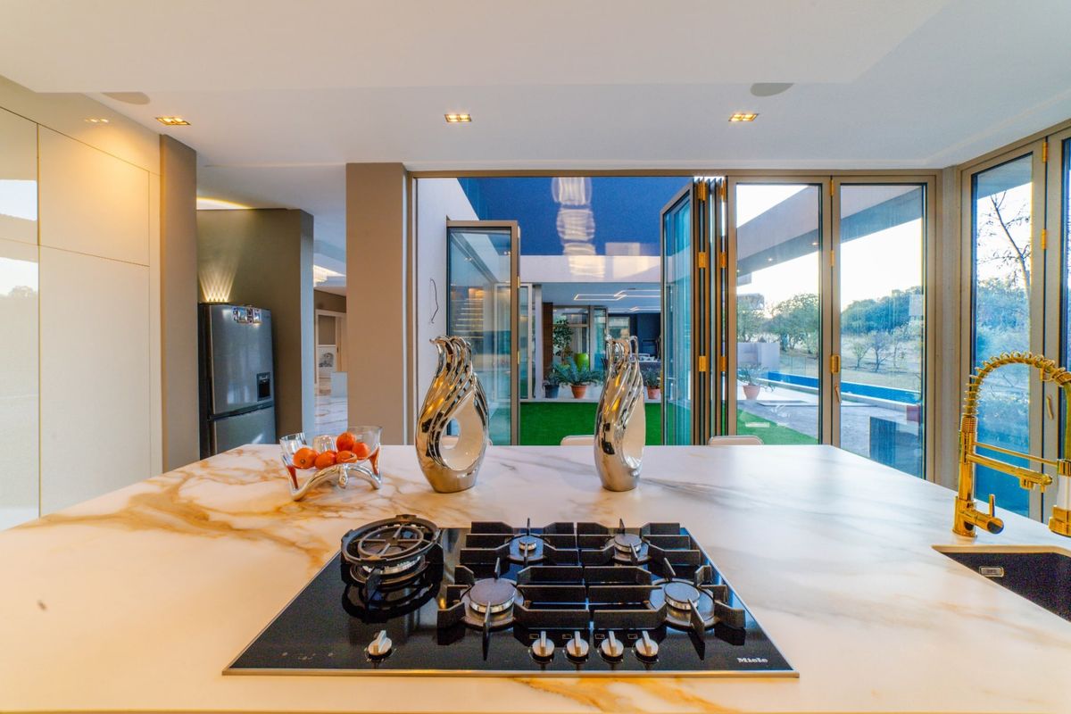 Modern kitchen featuring a marble island with a built-in gas hob, gold-tone faucet, and seamless bi-fold doors opening to an outdoor patio and pool area.