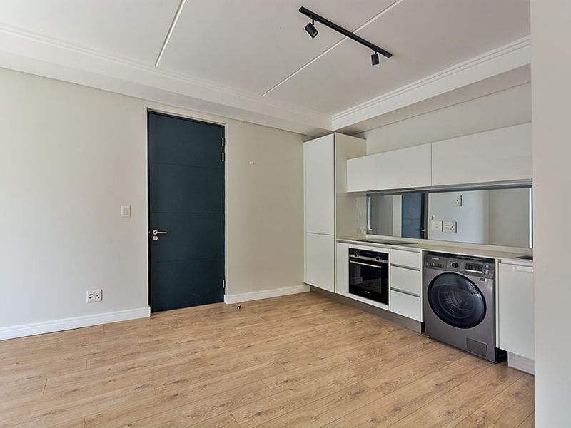 Modern kitchen featuring sleek white cabinetry, integrated oven and hob, mirror splashback, and durable laminate flooring in an open-plan layout.
