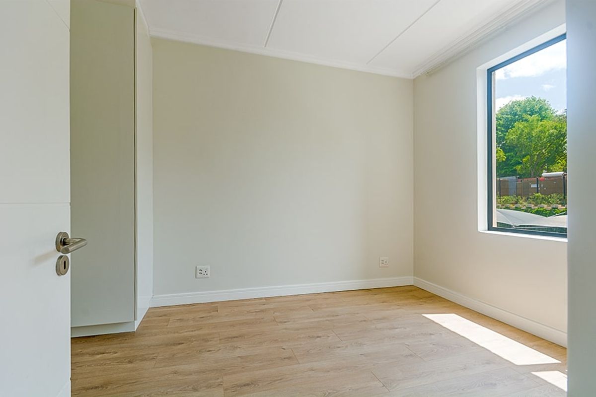 A bright, empty bedroom featuring modern laminate flooring, neutral walls, and a built-in cupboard with natural light from the window.