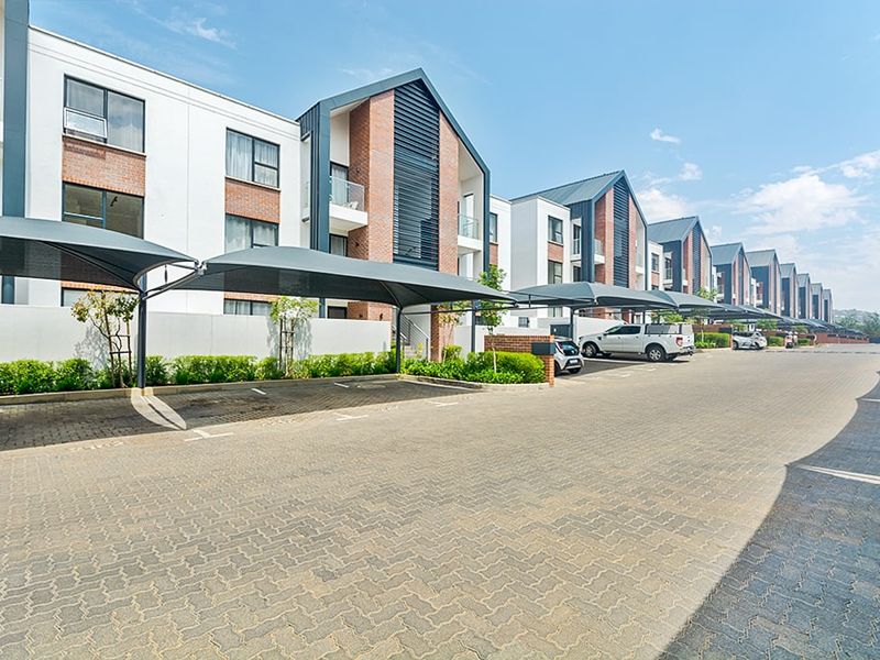 Modern apartment complex exterior featuring paved parking areas with shade sail carports and contemporary brick and white facade architecture.