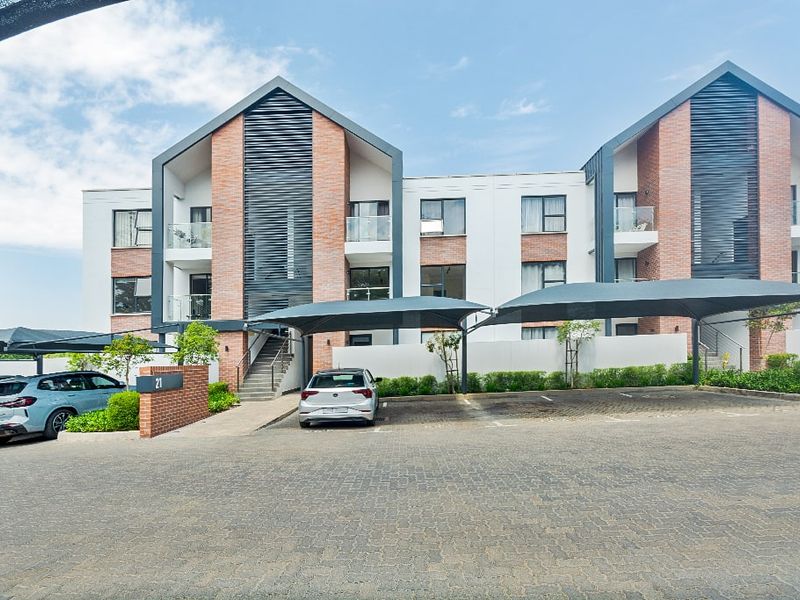 Front exterior view of a modern apartment complex featuring brick and white facade elements, covered parking bays, and paved driveway access.