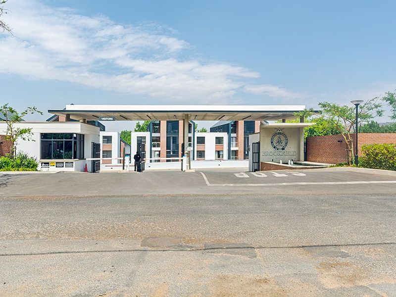 The main entrance and security gatehouse of the Brookfield apartment complex, featuring a paved driveway and modern architectural facade.