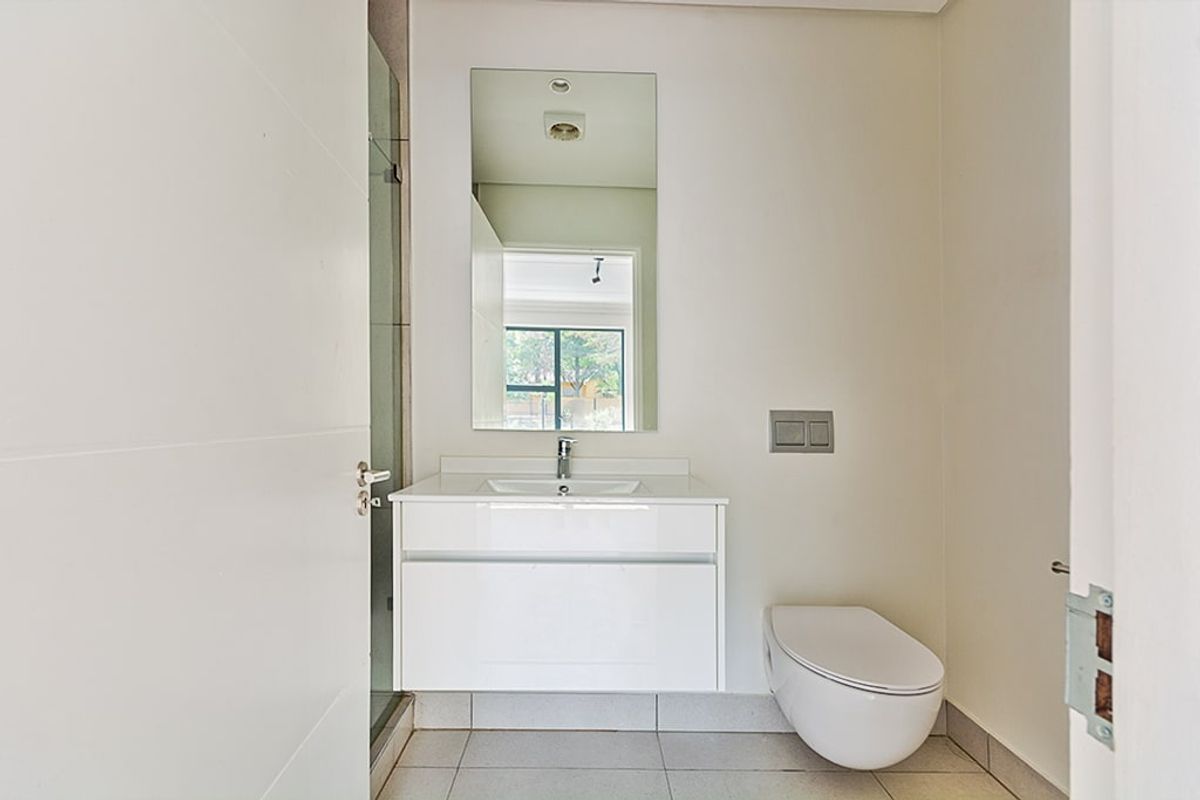 A modern, minimalist bathroom featuring a wall-hung vanity, wall-hung toilet, and a glass-enclosed shower with neutral floor tiling.