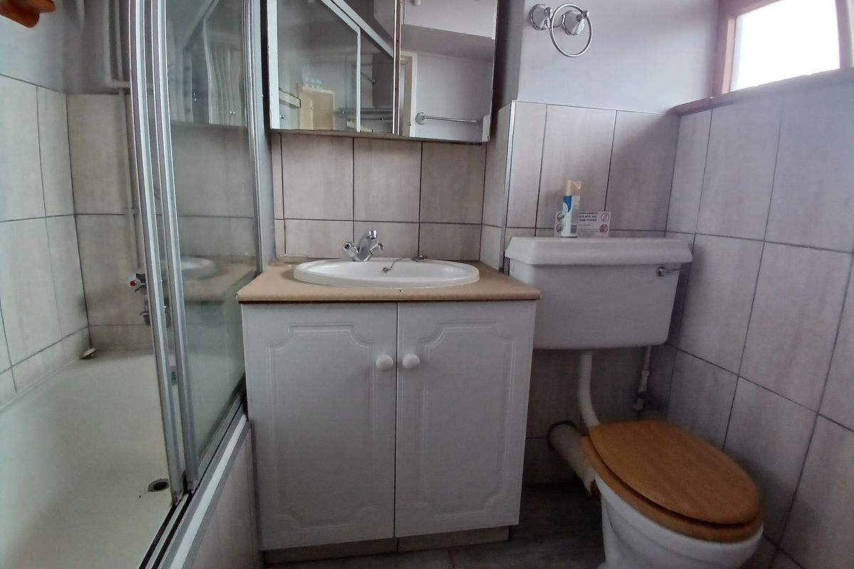 A functional bathroom featuring a shower-over-bath combination, a vanity unit with integrated basin, and a standard toilet with tiled wall finishes.
