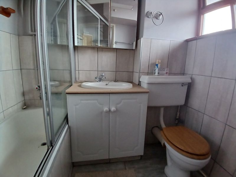 A functional bathroom featuring a shower-over-bath combination, a vanity unit with integrated basin, and a standard toilet with tiled wall finishes.