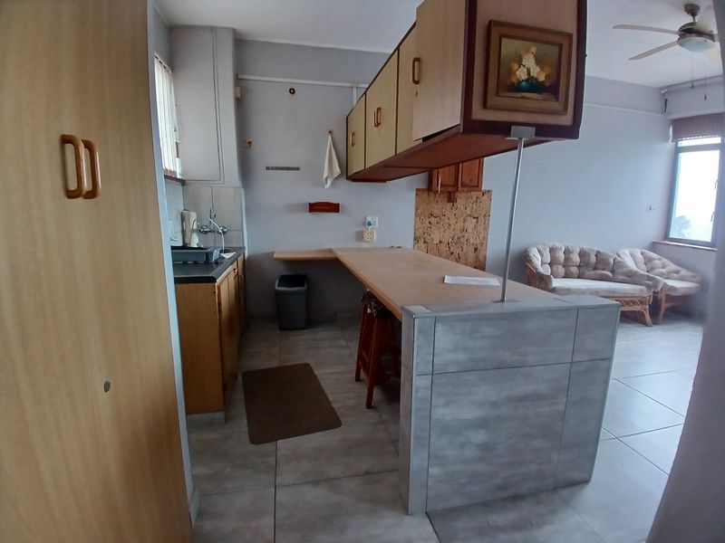 Open-plan kitchen and living area featuring a breakfast bar, tiled flooring, and built-in cabinetry, offering potential for modernization and layout optimization.