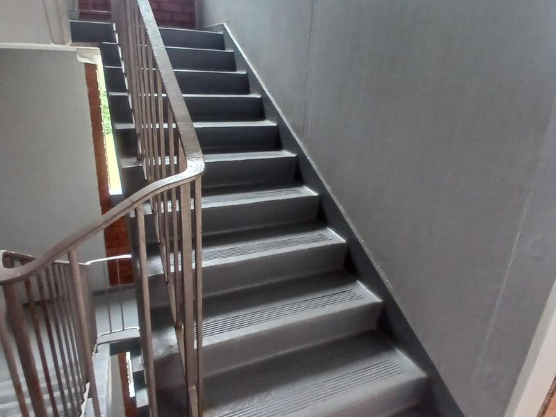A functional interior stairwell featuring painted concrete steps and a metal handrail, providing access between levels in the apartment building.