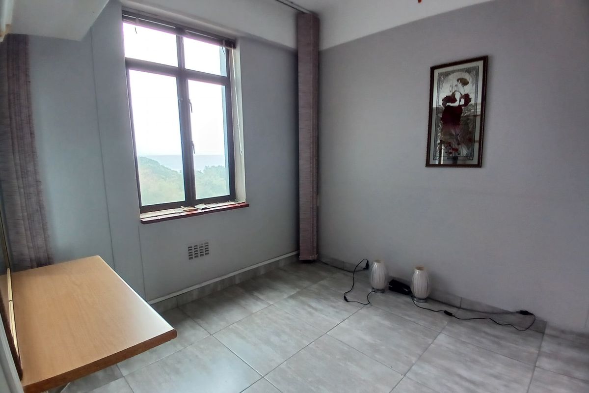 A bright, empty bedroom featuring neutral tiled flooring and a large window with natural light, offering a clean canvas for interior design.