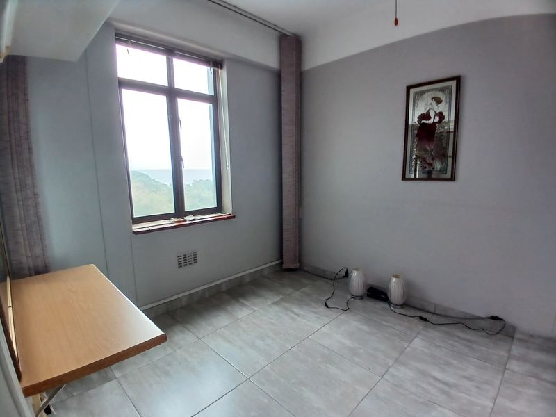 A bright, empty bedroom featuring neutral tiled flooring and a large window with natural light, offering a clean canvas for interior design.
