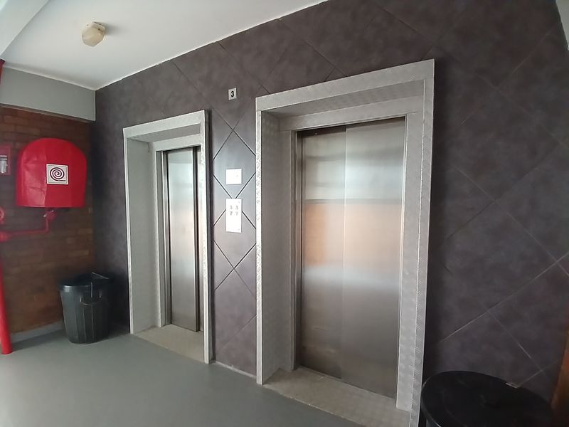 A clean apartment building hallway featuring dual stainless steel elevators, a fire hose reel, and a modern tiled feature wall.