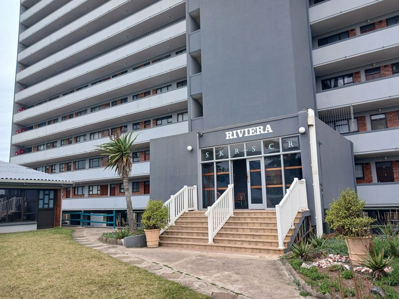 The front entrance of the Riviera apartment building, featuring a tiled staircase with white balustrades and a modern glass-fronted lobby area.
