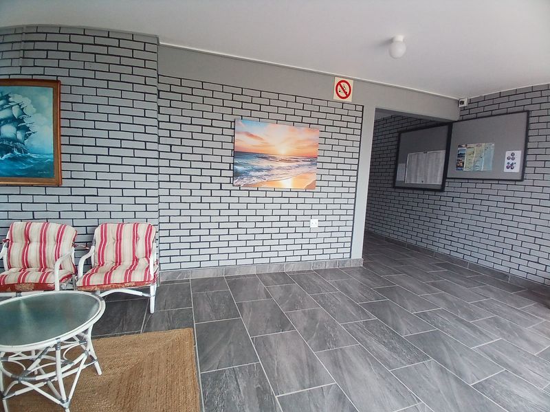 A clean and well-maintained apartment building entrance lobby featuring grey brickwork walls and modern grey floor tiles.