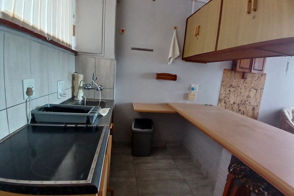 A dated kitchen featuring built-in cabinetry, an electric hob, a stainless steel sink, and a breakfast bar area with tiled flooring.