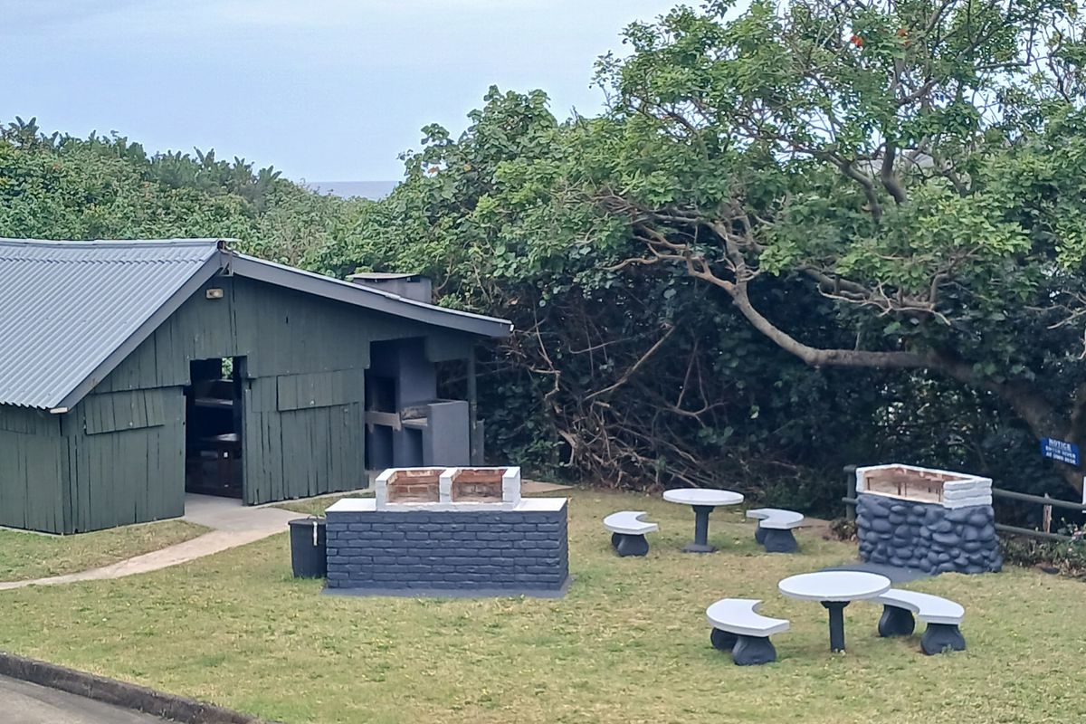 Outdoor communal area featuring built-in braai facilities, stone masonry, and a timber-clad structure set within a landscaped garden environment.