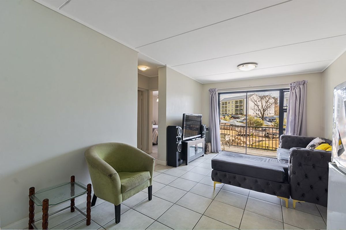 A bright living room featuring tiled flooring and a sliding glass door that provides access to a balcony with exterior views.