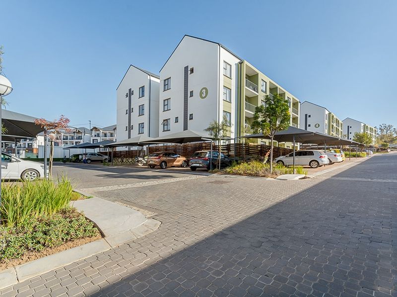 Exterior view of a modern apartment complex featuring paved driveways, covered parking bays, and well-maintained landscaped garden areas.