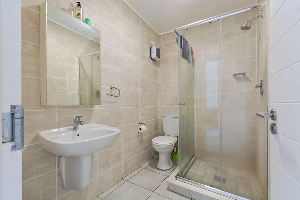 A functional bathroom featuring a pedestal basin, toilet, and a glass-enclosed shower with neutral wall and floor tiling.