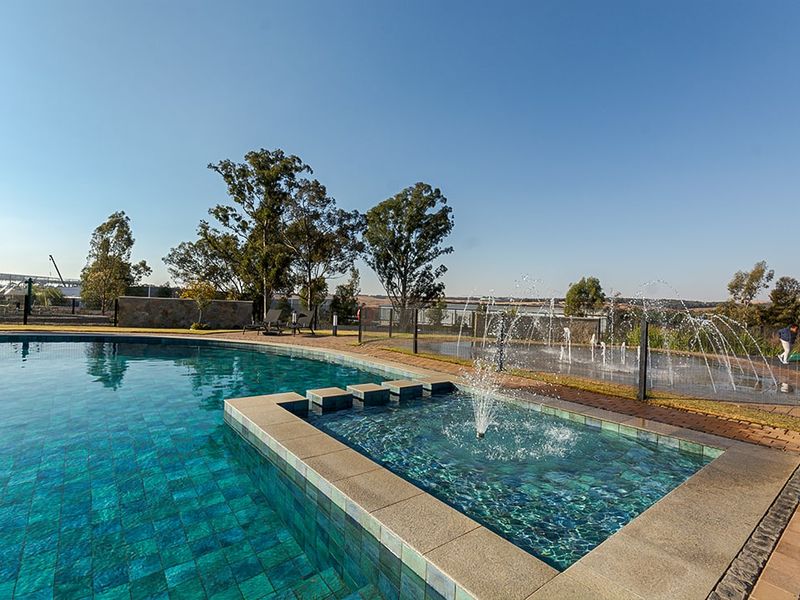 A well-maintained outdoor swimming pool area featuring a built-in water fountain, paved surround, and secure perimeter fencing.