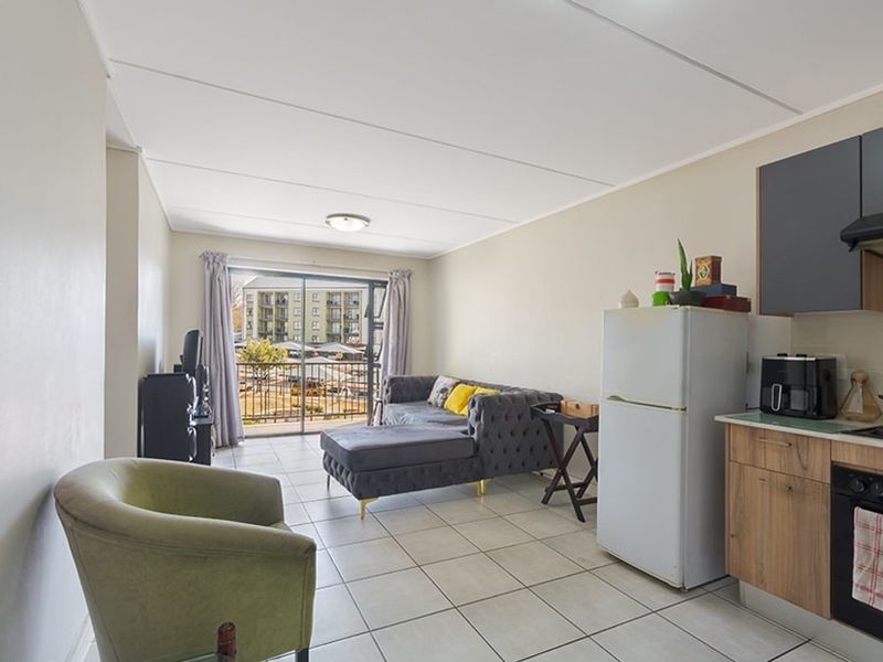 Open-plan living area featuring tiled floors, a compact kitchen with built-in cabinetry and appliances, and a sliding door leading to a balcony.