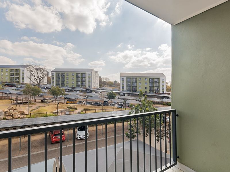 A private balcony featuring a metal balustrade with an elevated view overlooking the apartment complex grounds and parking area.