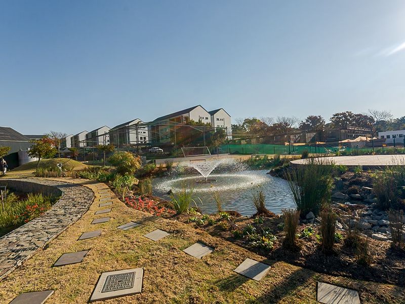 A well-maintained communal garden area featuring a central water fountain, stone pathways, and landscaped greenery within an apartment complex.