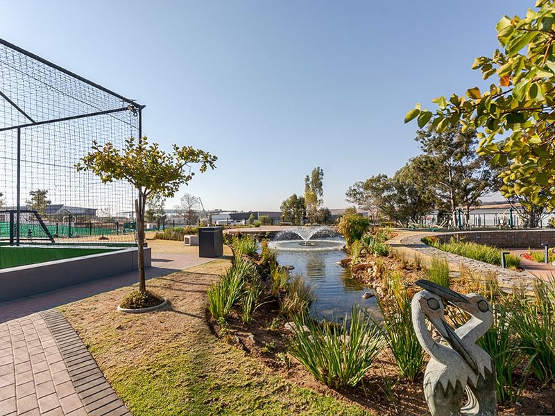 A well-maintained communal garden area featuring a central water fountain, paved walkways, and sports facility netting.