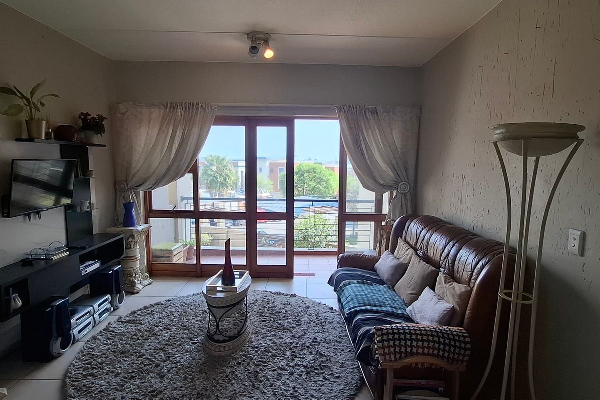 A living room featuring tiled flooring and a sliding glass door providing access to a balcony, with visible wall plaster cracks.