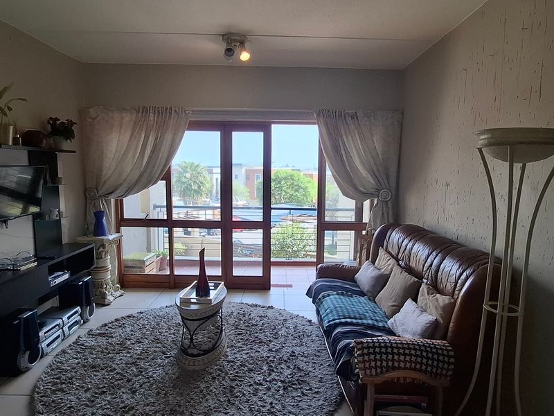 A living room featuring tiled flooring and a sliding glass door providing access to a balcony, with visible wall plaster cracks.