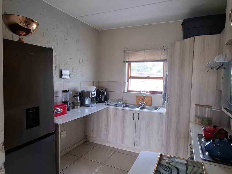 A functional kitchen featuring light wood-grain cabinetry, tiled flooring, a double sink, and integrated cooking appliances, requiring minor wall repairs.