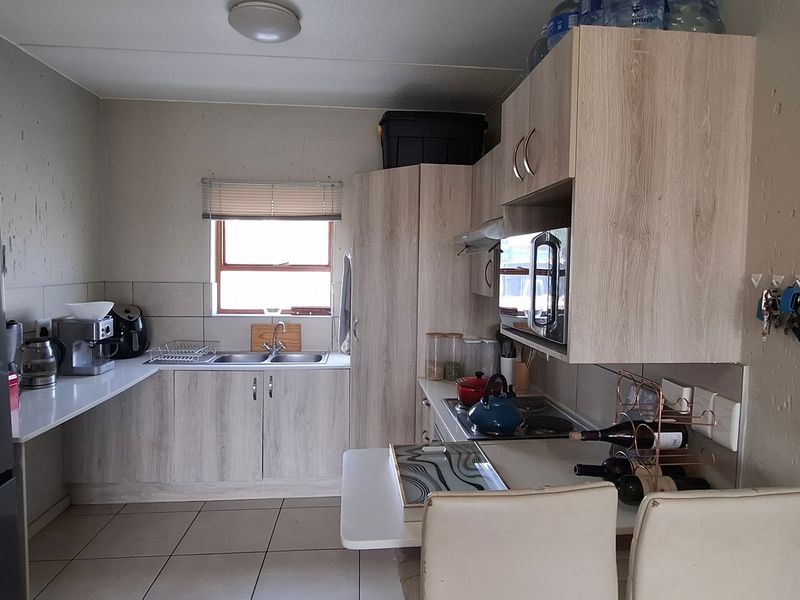 Functional kitchen featuring light wood-look cabinetry, tiled flooring, a double basin sink, and built-in appliances including a microwave and cooktop.