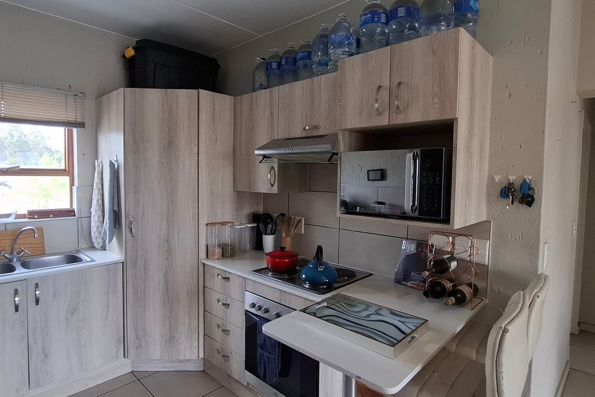 Compact kitchen featuring light wood-grain cabinetry, integrated appliances including an oven and hob, stainless steel sink, and tiled backsplash.