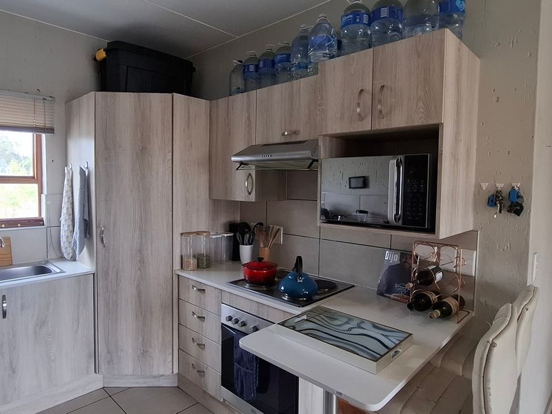 Compact kitchen featuring light wood-grain cabinetry, integrated appliances including an oven and hob, stainless steel sink, and tiled backsplash.